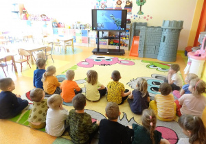 Dzieci oglądają prezentację multimedialną na temat dinozaurów.